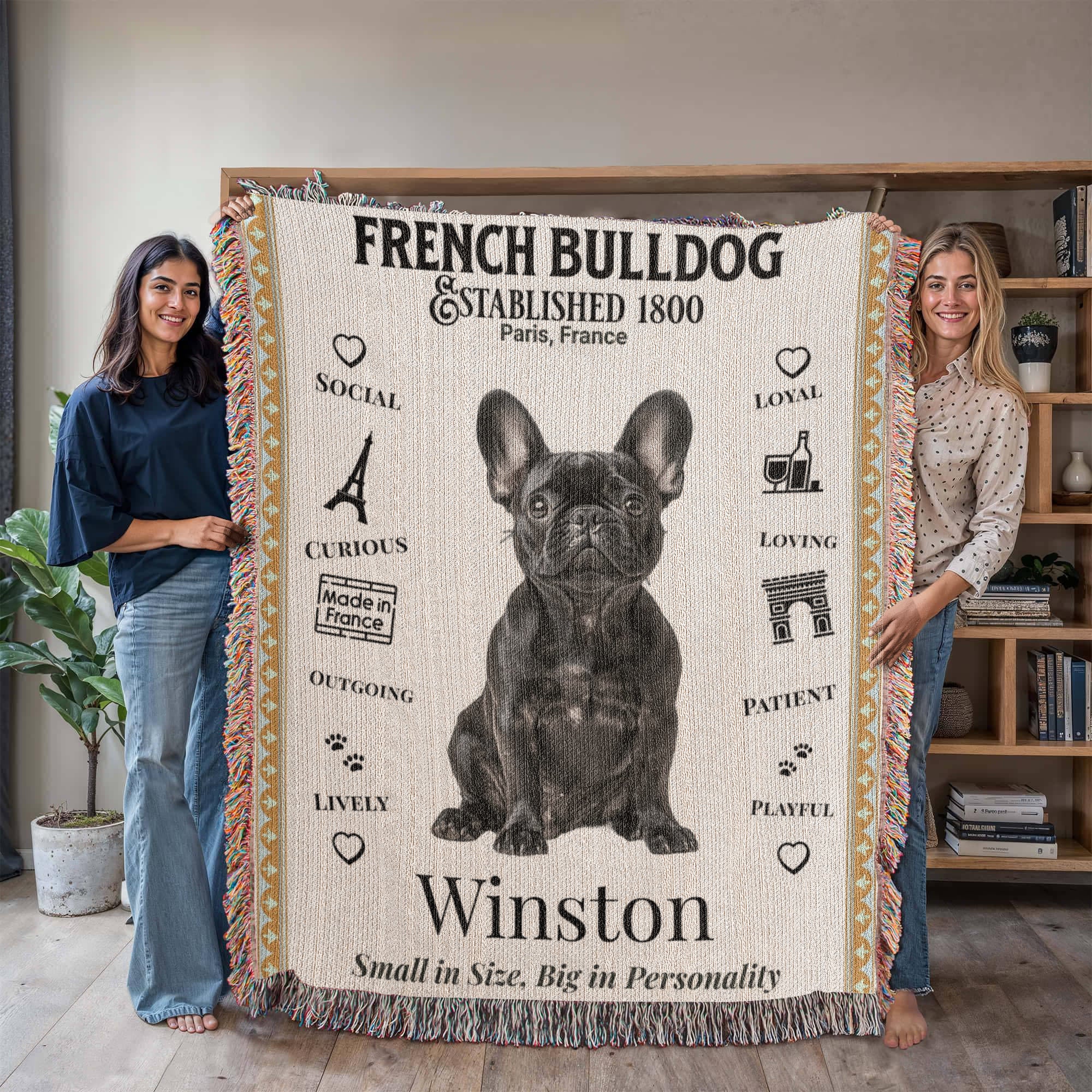 Two people holding a French Bulldog-themed blanket with illustrations and text.Personalized with your Frenchie's name and photo.