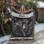 Person holding a decorative tarot card pitbull blanket with a dog design and 'Max' printed on it, outdoors with snow and flowers.