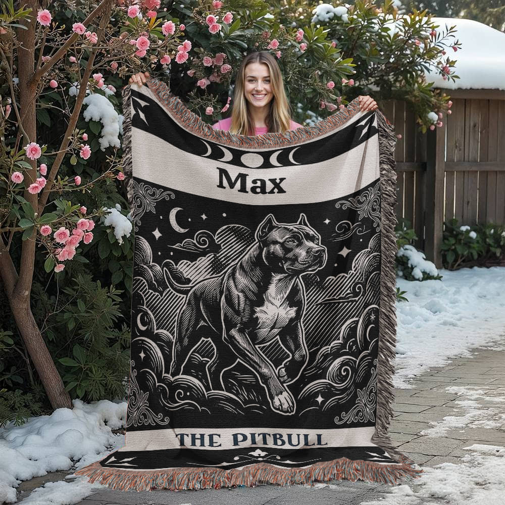 Person holding a decorative tarot card pitbull blanket with a dog design and 'Max' printed on it, outdoors with snow and flowers.
