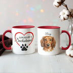 Two mugs with red interiors and handles, one featuring a dachshund illustration and text, on a light wooden surface.