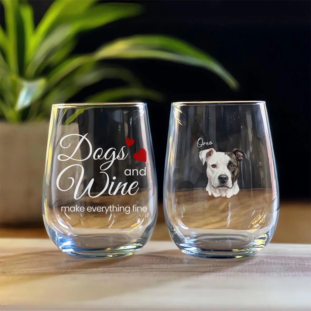 Two stemless wine glasses with one featuring 'Dogs and Wine make everything fine' text and the other with a dog's face, on a wooden surface.