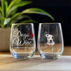 Two stemless wine glasses with one featuring 'Dogs and Wine make everything fine' text and the other with a dog's face, on a wooden surface.