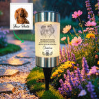 A custom dog memorial garden stake lamp shown outdoors in a garden during rain. The cylindrical lamp features a printed illustration of a dachshund and the text 
