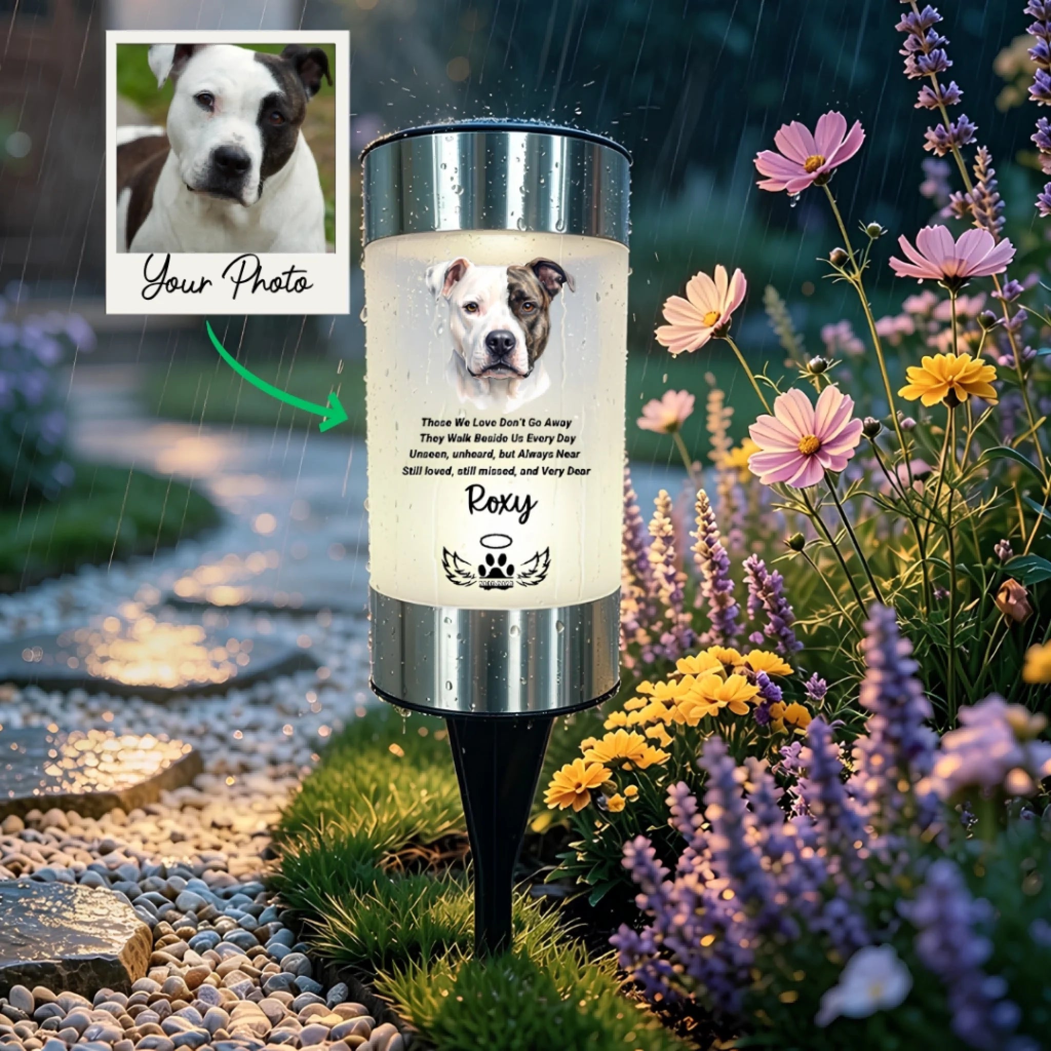 A custom pet memorial garden light shown in a rainy garden setting. The cylindrical light has a silver metal top and bottom, a glowing white center, and a black stake.