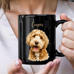 A person holding a glossy black ceramic mug with a custom printed design of a golden doodle dog and the name 'Cooper' in gold script.