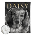 A personalized pet blanket featuring a black and white photograph of a dachshund with the name 'DAISY' printed in gold at the top. A circular inset in the bottom-left corner shows the soft white sherpa backing of the blanket.
