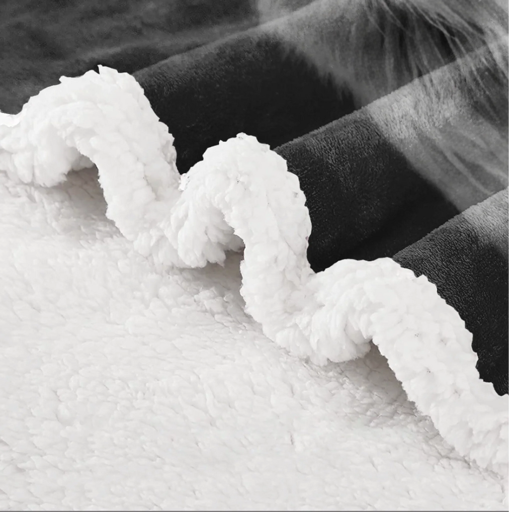 Close-up of a plush fleece blanket with a white sherpa-like underside and a dark charcoal/black top side, folded to show the soft texture.