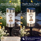 A split-screen comparison showing a solar-powered garden light in daylight on the left and at night on the right. The cylindrical lamp has a white body with black text and illustration, a dark blue solar panel on top, and a black stake.