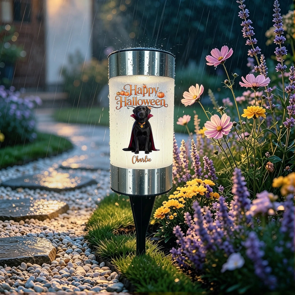 A cylindrical solar garden light with a black dog and 'Happy Halloween' graphic, set in a garden pathway during a rainy evening.