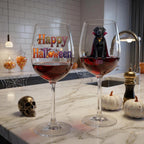 Two clear wine glasses filled with red wine sit on a marble kitchen counter. One glass has a colorful 'Happy Halloween' design, and the other has a black cat in a vampire cape with the name 'COCO' printed below.