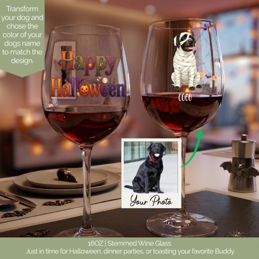 Two personalized 16oz stemmed wine glasses on a dining table, one with a colorful 'Happy Halloween' design and the other featuring a mummy dog graphic with the name 'Cleo'. A photo of a black Labrador retriever is shown in an inset box with a green arrow pointing to the right glass.