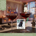 Two personalized 16oz stemmed wine glasses on a dining table, one with a colorful 'Happy Halloween' design and the other featuring a mummy dog graphic with the name 'Cleo'. A photo of a black Labrador retriever is shown in an inset box with a green arrow pointing to the right glass.