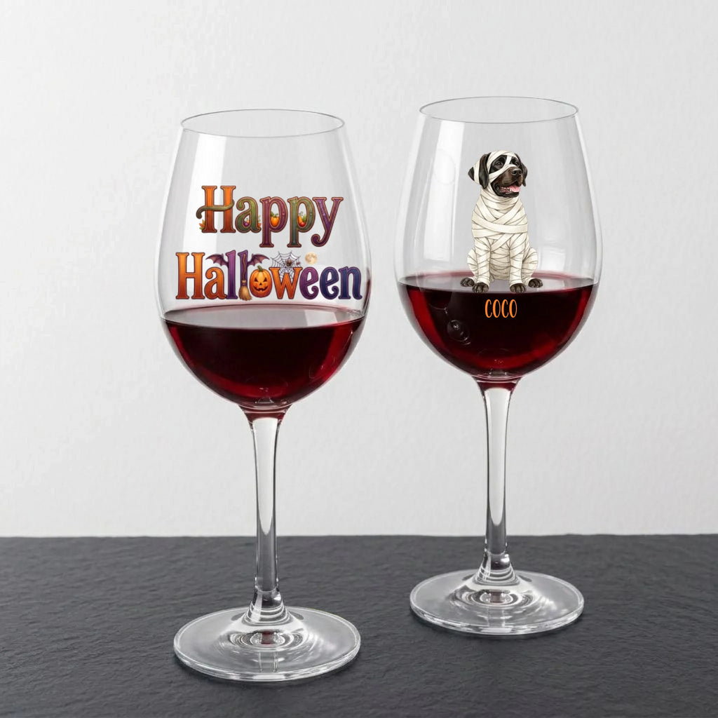 Two clear wine glasses filled with red wine, shown on a dark surface against a light gray background. The left glass has 'Happy Halloween' printed on it, and the right glass has a mummy dog illustration with the name 'COCO' near the base.
