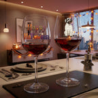 Two clear wine glasses filled with red wine on a dining table, decorated with Halloween-themed graphics. The left glass has 'Happy Halloween' in colorful letters, and the right glass features a cartoon mummy dog.
