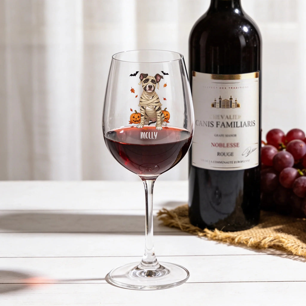 Personalized mummy-costume dog Halloween 16 oz wine glass with red wine next to a wine bottle and grapes