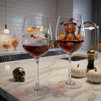 Two clear wine glasses filled with red wine sit on a marble kitchen counter. The left glass has a colorful 'Happy Halloween' decoration, and the right glass features a dachshund wearing a witch hat with pumpkins and the name 'DAISY'.