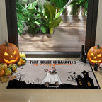 A Halloween-themed doormat featuring a French bulldog in a ghost costume, set in front of a glass door with pumpkins and fall decorations around it.