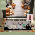 A Halloween-themed luxury door mat featuring two French bulldogs in ghost costumes with the text 'THIS HOUSE IS HAUNTED by a very ghostly dog and you'. The mat is displayed on a wooden porch surrounded by pumpkins, spiders, and a black raven, with a 'Your Photo' customization inset showing a real dog portrait transformed into the ghost dog design.
