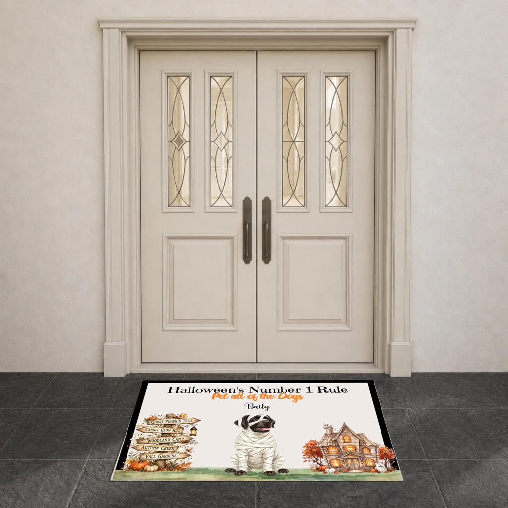 A rectangular Halloween-themed doormat placed in front of double cream-colored front doors. The mat features the text 'Halloween's Number 1 Rule.