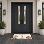 A rectangular front door doormat with a Halloween-themed illustration and the text 'Halloween Number 1 Bole' and 'Stay in the Fun' is placed in front of dark charcoal double front doors on a tiled entryway floor, flanked by potted plants and wall sconces.