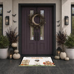 A Halloween-themed doormat with illustrations of a haunted house, a skull, and the text 'Halloween Number 1 Rule: Stay Home' is displayed on a dark tiled entryway floor in front of a dark purple double door decorated with a wreath, pumpkins, and lanterns.