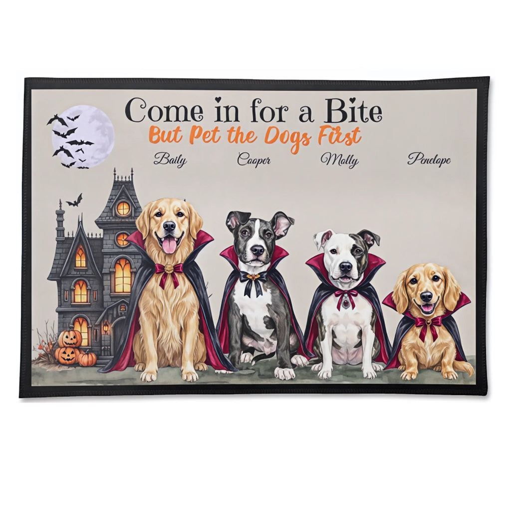 A rectangular doormat with a black border featuring a Halloween-themed illustration of four dogs in vampire capes in front of a haunted house and full moon. The text reads 'Come in for a Bite But Pet the Dogs First' with customizable dog names below.