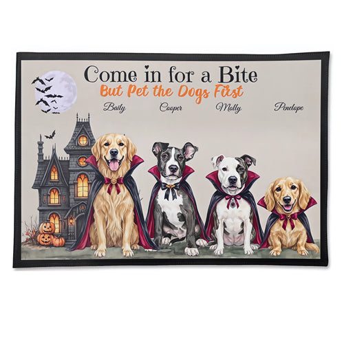 A rectangular doormat with a black border featuring a Halloween-themed illustration of four dogs in vampire capes in front of a haunted house and full moon. The text reads 'Come in for a Bite But Pet the Dogs First' with customizable dog names below.