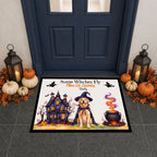 A rectangular Halloween-themed doormat displayed in front of a dark blue door, surrounded by fall decorations including pumpkins, lanterns, and autumn leaves. The mat features an illustration of a golden retriever dog in a witch hat next to a haunted house and a bubbling cauldron, with the text 'Some Witches Fly Mine Or Yours Daily'.