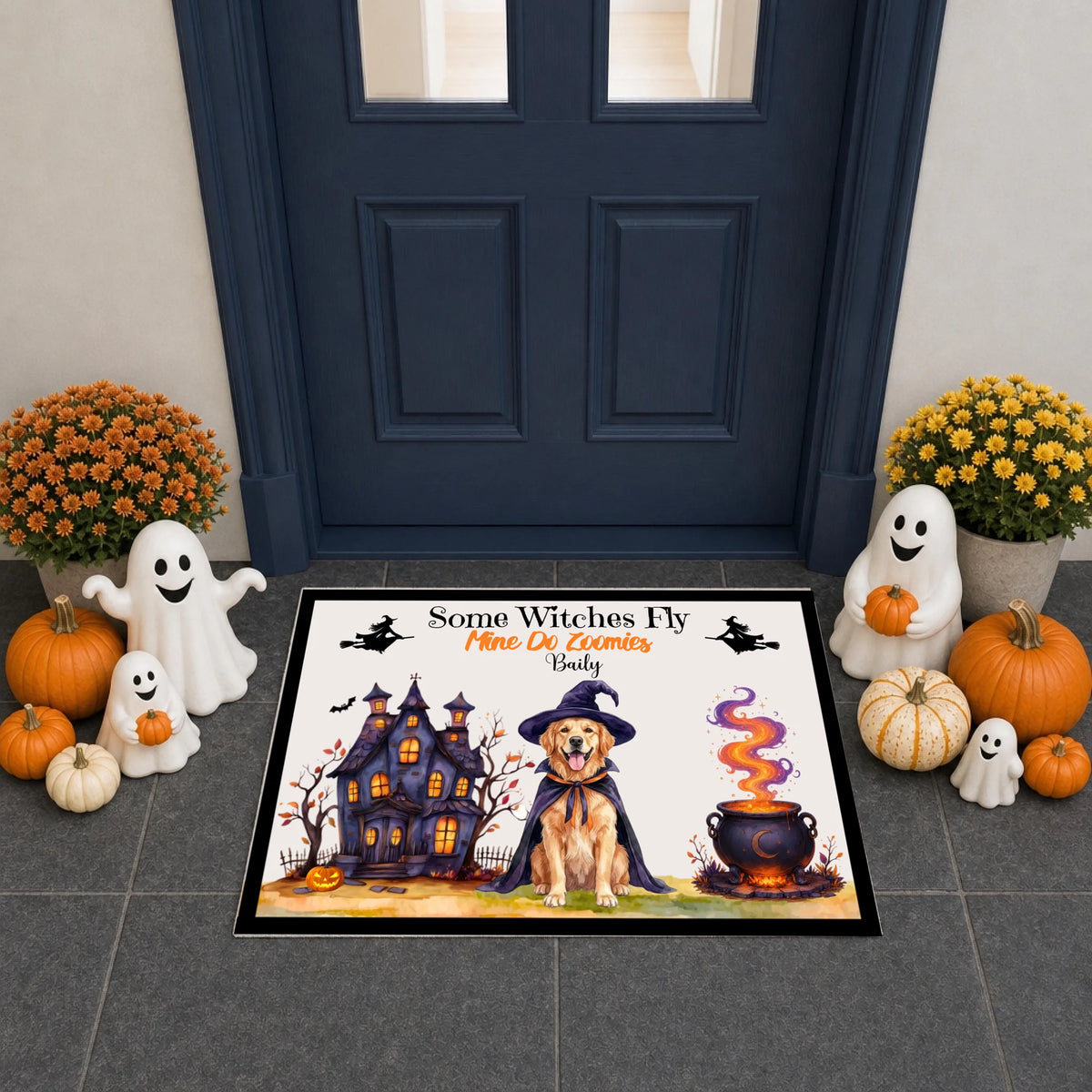 A rectangular Halloween doormat with a colorful illustration of a golden dog in a witch hat, a haunted house, a cauldron, and ghost figures, placed in front of a dark blue door with pumpkins, white ghost decorations, and yellow flowers around it.