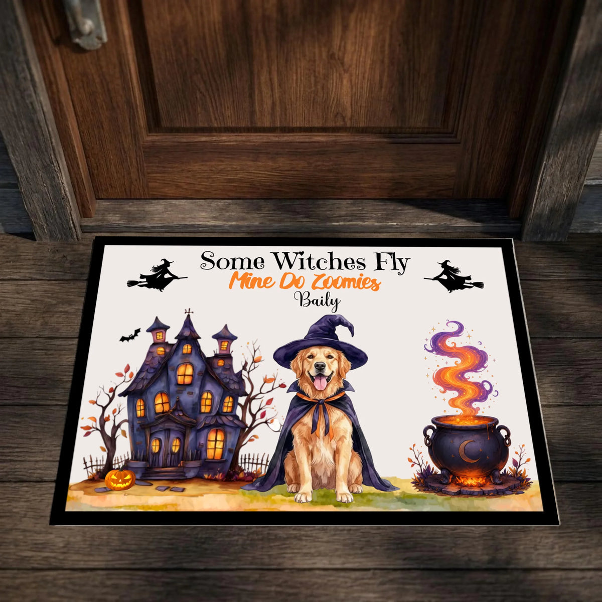 A rectangular Halloween doormat placed in front of a dark wooden door. The mat features a cartoon illustration of a golden retriever dog in a witch hat beside a haunted house and a bubbling cauldron, with the text 'Some Witches Fly Mine Do Lummies Badly'.