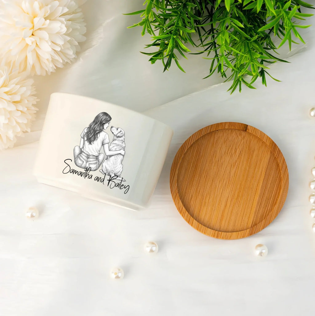 A white ceramic keepsake jar with a custom black line art illustration and the text 'the Samantha and Kathy' on the front, shown next to its round bamboo lid on a white marble surface with decorative flowers, greenery, and pearls.