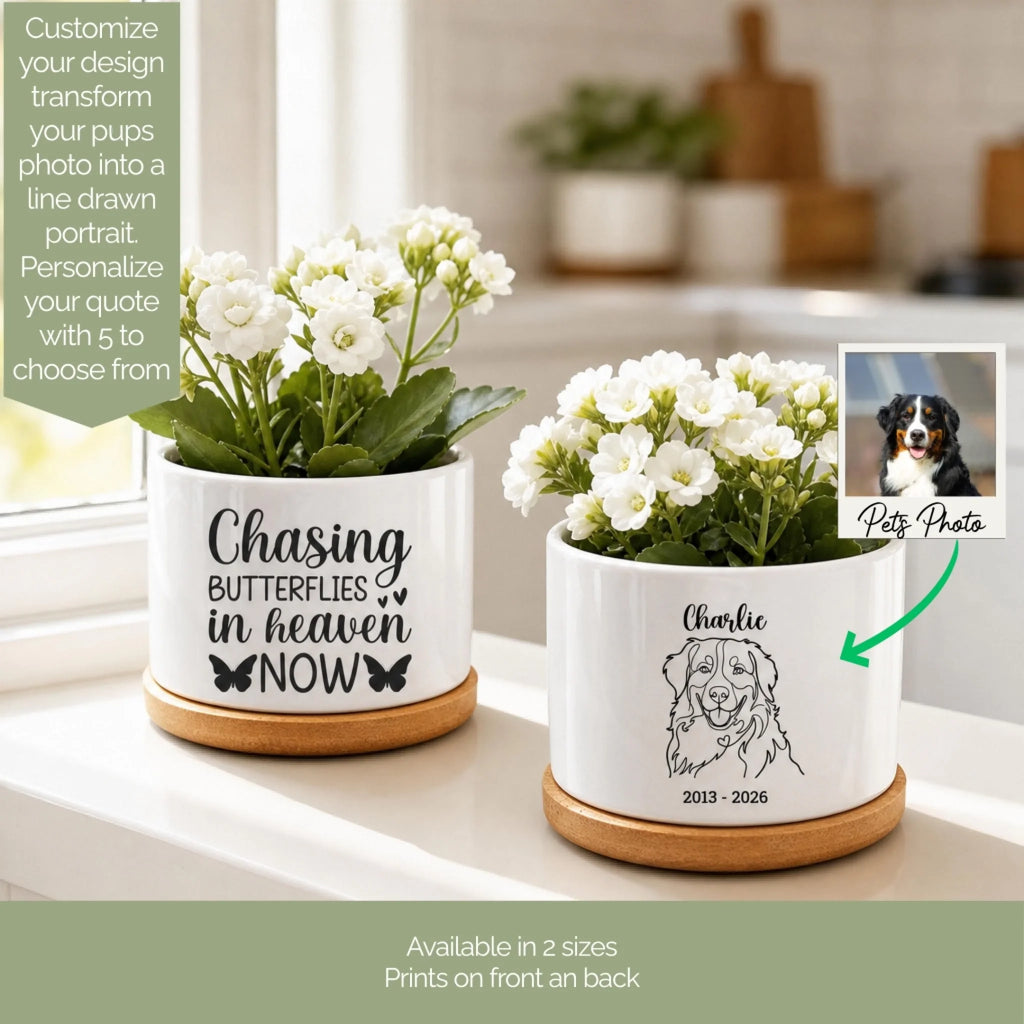 Two white ceramic pet memorial planters with wooden bases displayed on a windowsill. One planter features a customizable quote 'Chasing Butterflies in Heaven Now' with butterfly graphics, and the other is personalized with the name 'Charlie' and a dog illustration.
