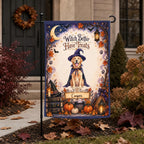 A Halloween garden flag displayed on a black metal stand in a yard. The flag features an illustrated golden retriever wearing a witch hat and cape, surrounded by pumpkins, autumn leaves, a witch hat, a broom, and the text 'Witch Better Have Treats' with a personalized nameplate reading 'Cooper'.