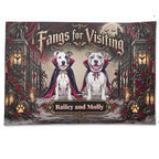 A rectangular printed banner or sign featuring two white pitbull-type dogs dressed as vampires in red and purple cloaks, standing in a gothic courtyard with pumpkins, roses, lanterns, and the text 'Fangs for Visiting' and 'Bailey and Molly'.
