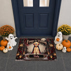 A Halloween-themed doormat featuring a golden retriever dressed as a vampire, surrounded by ghosts, pumpkins, and a haunted gate. The mat is displayed on a gray tiled floor in front of a dark blue door, flanked by decorative pumpkins and ghost figurines.