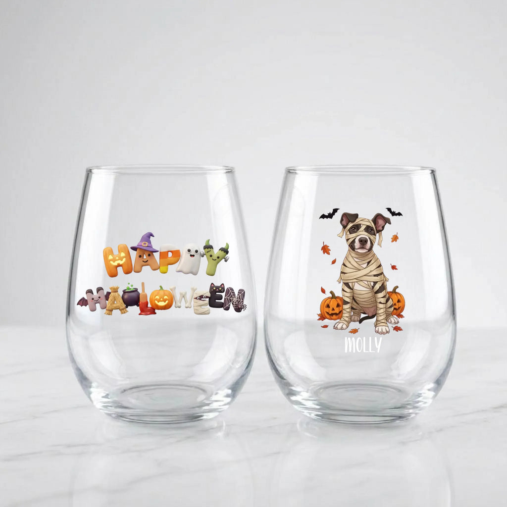 Two personalized Halloween stemless wine glasses on marble, one with 'Happy Halloween' lettering, one with a mummy-costume dog with pumpkins and pet name