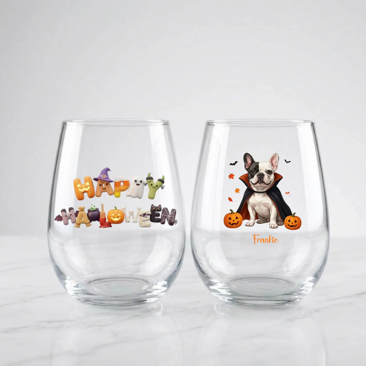 Two personalized Halloween stemless wine glasses on marble, one with 'Happy Halloween' lettering, one with a vampire-costume dog with pumpkins and pet name