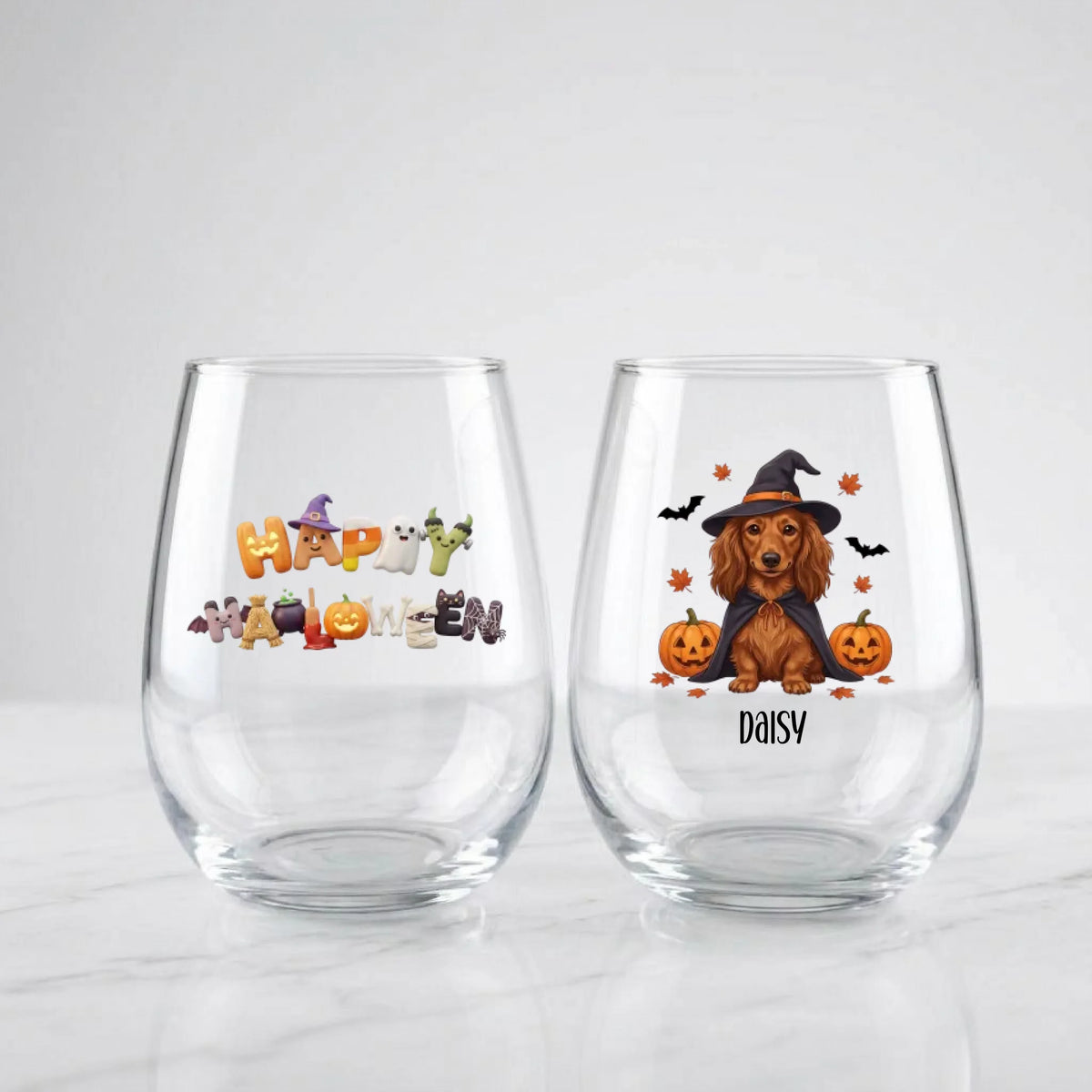 Two personalized Halloween stemless wine glasses on marble, one with 'Happy Halloween' lettering, one with a witch-costume dog with pumpkins and pet name
