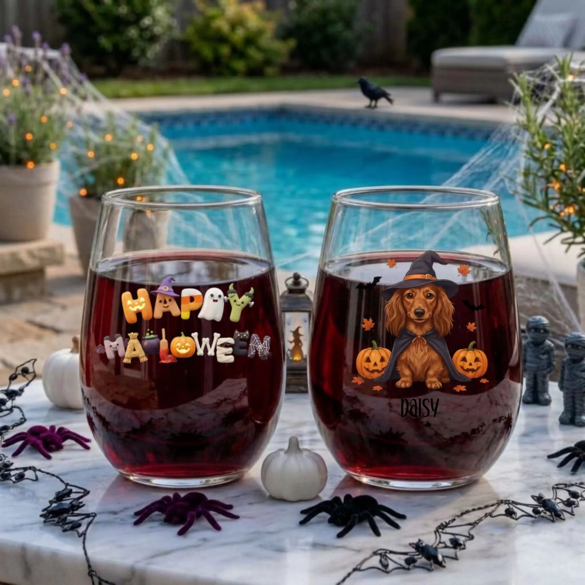 Two personalized Halloween stemless wine glasses filled with red wine on a poolside table, one with a witch-costume dog with pumpkins