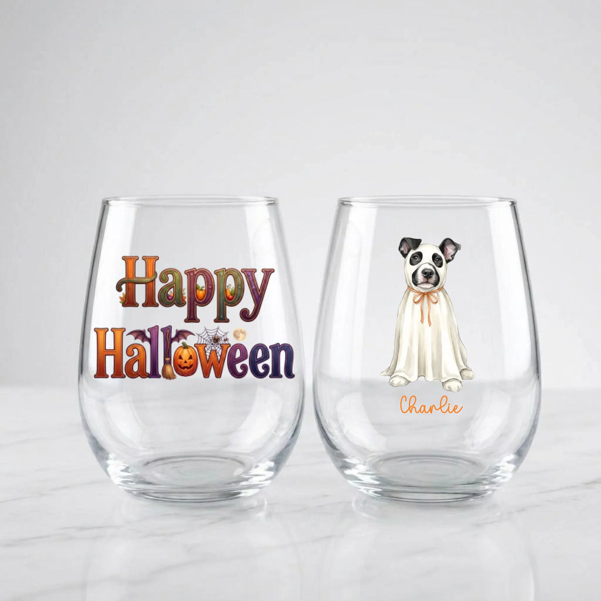 Two personalized Halloween stemless wine glasses on marble, one with 'Happy Halloween' lettering, one with a watercolor ghost-costume dog and pet name