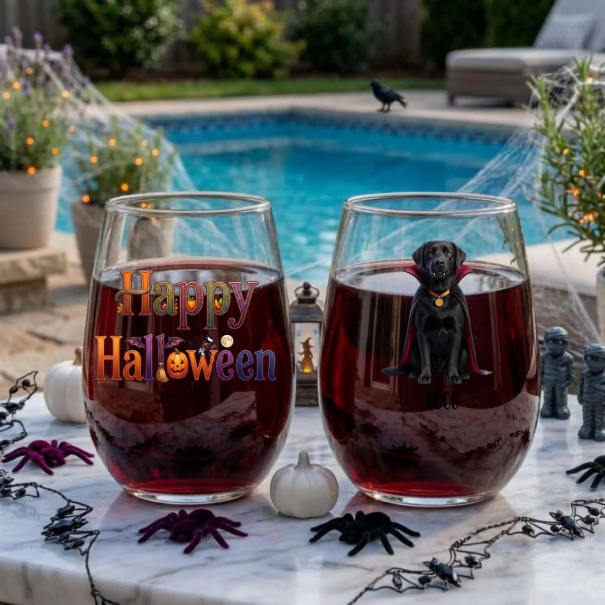 Two personalized Halloween stemless wine glasses filled with red wine on a poolside table, one with a watercolor vampire-costume dog