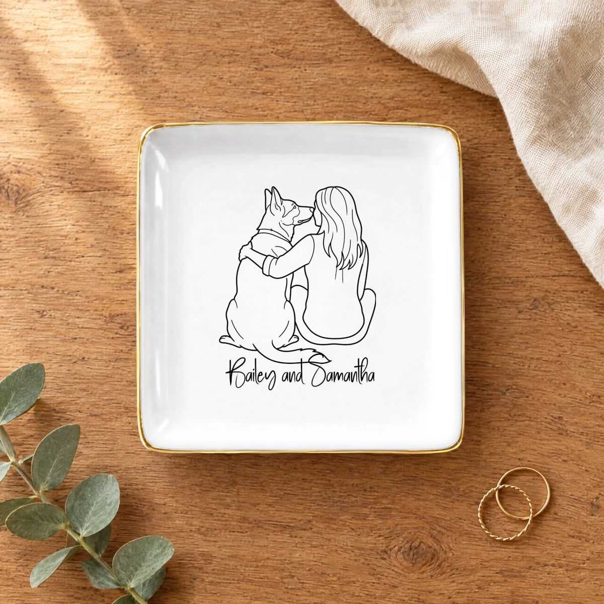 Line drawing person and dog square ring dish on a wooden table with linen and eucalyptus