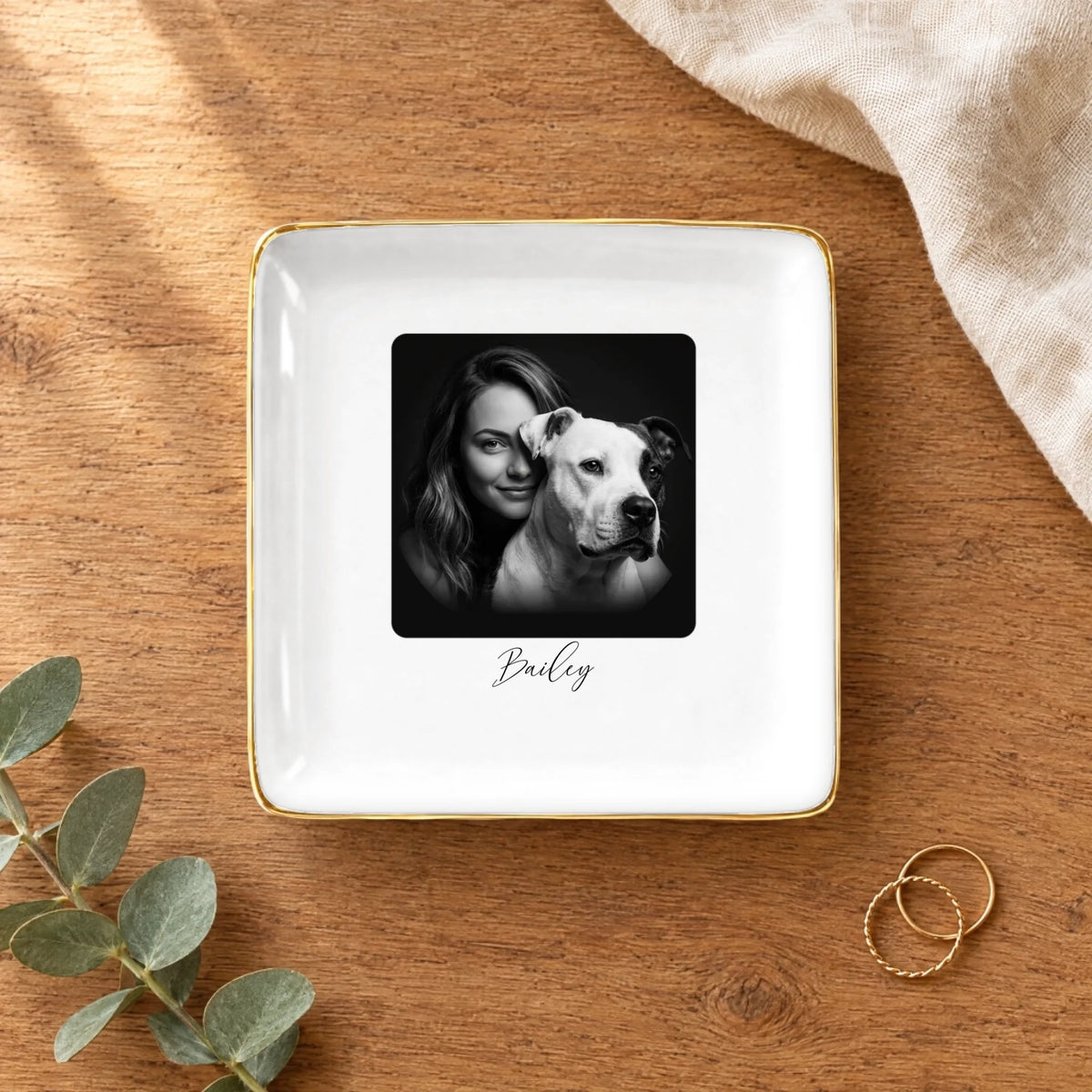 Black and white studio portrait square ring dish on a wooden table with linen and eucalyptus