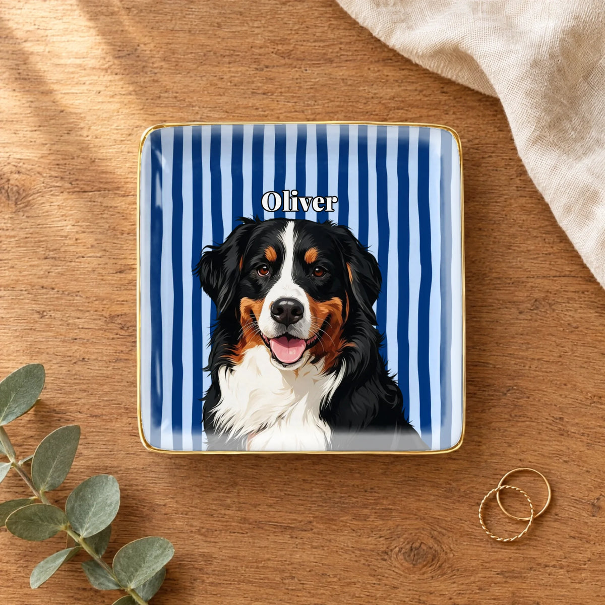 Square striped pet portrait ring dish on a wooden table with linen and eucalyptus