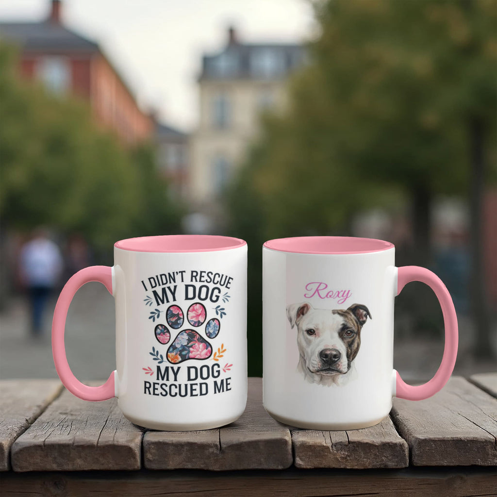 Two mugs with pink handles on a wooden surface, one featuring a dog rescue message and the other with a dog's face.