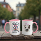 Two mugs with pink handles on a wooden surface, one featuring a dog rescue message and the other with a dog's face.