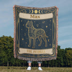 Person holding a decorative woven blanket with a tarot card dog design and personalized with the name 'Max' printed on it, outdoors.