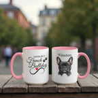 Two mugs with pink interiors and handles on a wooden surface, one featuring text and the other a dog illustration.