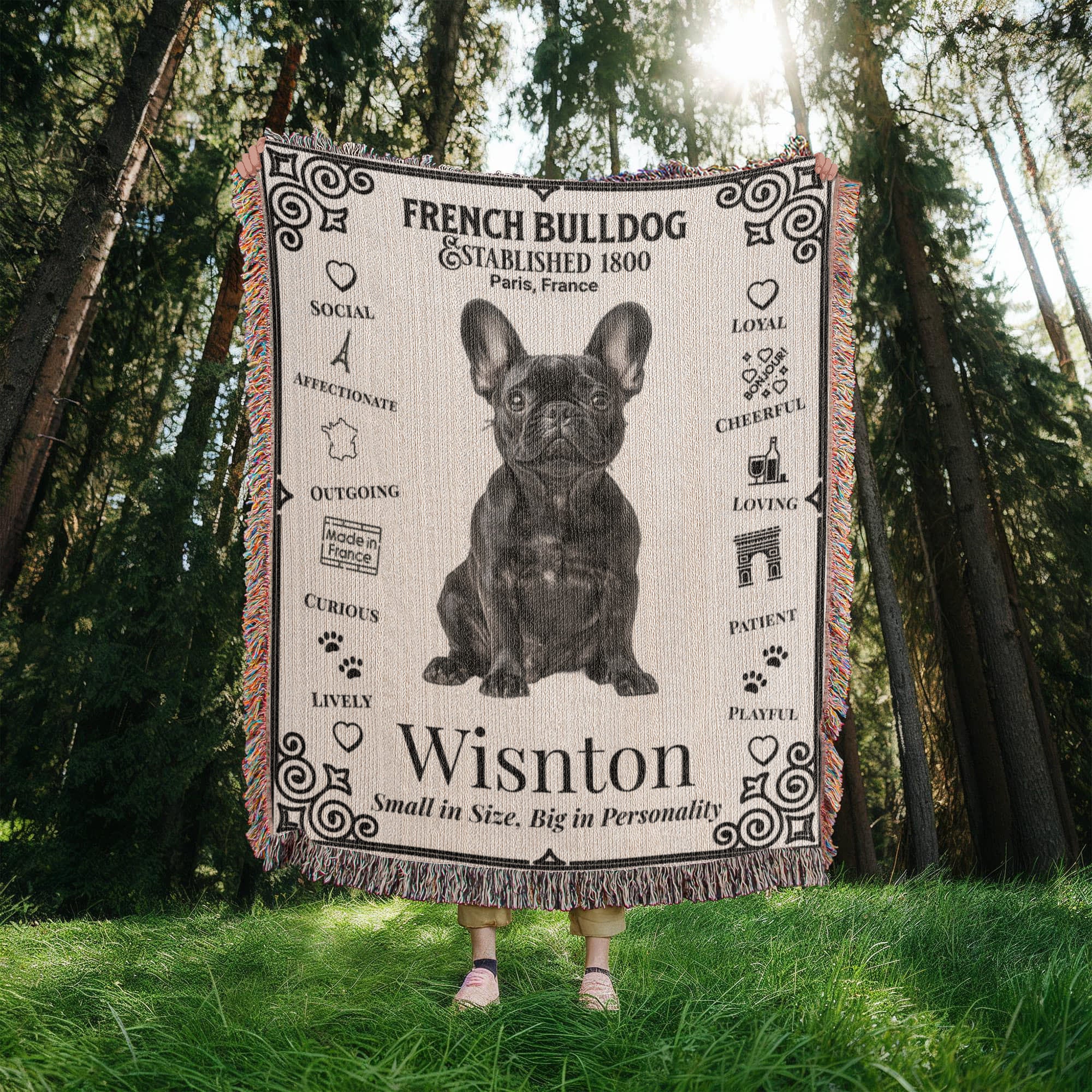 Person holding a French Bulldog-themed blanket with text and graphics in a forest setting.Personalized with your Frenchie's photo and name.