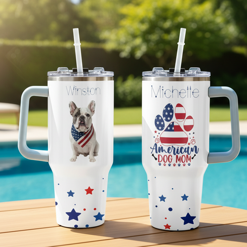 Two insulated travel mugs with handles, one featuring a dog and the other with 'American Dog Mom' text and designs, on a table.